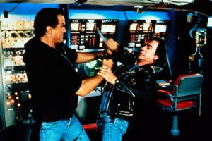 Two men fight in a sci-fi cockpit, grappling amid glowing control panels and screens.
