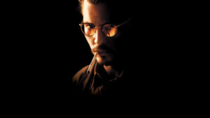 Close-up of a man with round glasses smoking a cigarette in a dark, warm-lit setting.