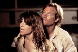 Two soaked adults in beige shirts look alarmed as they cling together in a dim setting, faces lit with worry.