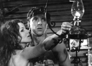 Man and woman adjust a vintage hanging oil lamp in a dim workshop.