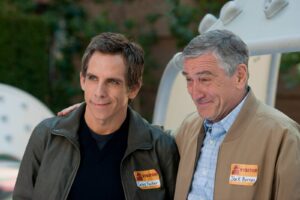 Two men wearing jackets with orange and white visitor badges smile for the camera outdoors; badges read Greg Focker and Jack Byrnes.