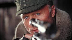 Man wearing a dark green cap aims a rifle, eyes fixed on the target.