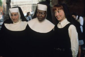 Three nuns walking together in black habits with white coifs, appearing outdoors, with the middle nun looking surprised.
