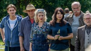 Group of six adults standing outdoors in a park-like setting, facing the camera.