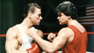 Two male boxers face off in a ring, wearing white and red singlets and red gloves, staring each other down.