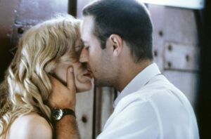 Man and woman share a kiss, his hand cupping her cheek as they lean in closely.