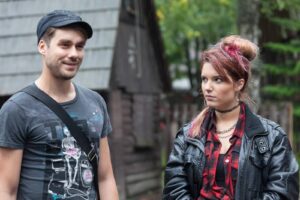 Two young adults standing in the rain outdoors, facing each other in casual outfits.