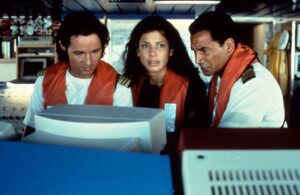 Three crew members in white uniforms with orange life vests gathered around a large computer console.