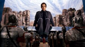 Man in dark jacket perched over a row of armored soldiers, set against canyon backdrop; tense moment as he looks down.