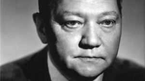 Black-and-white close-up portrait of a man’s face, cropped to show from the nose to the jaw in a formal suit.