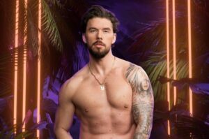 shirtless man with a beard and necklace poses in neon tropical backdrop with orange light bars and palm leaves.