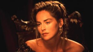 Woman with an elegant updo and gold earrings gazes pensively in warm, dim lighting.
